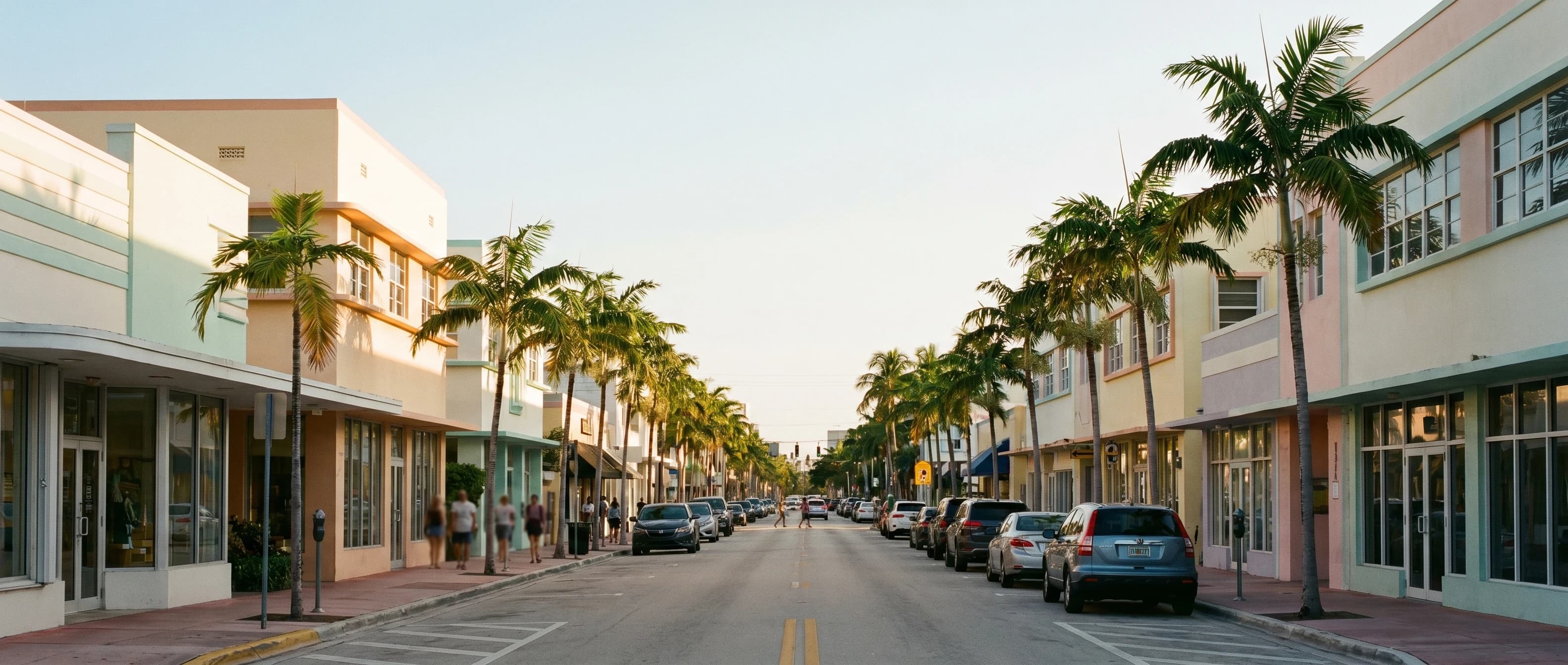 Wide view of a Downtown Delray Beach commercial corridor at warm evening light — palm trees and low-rise mid-century storefronts on both sides of the street.